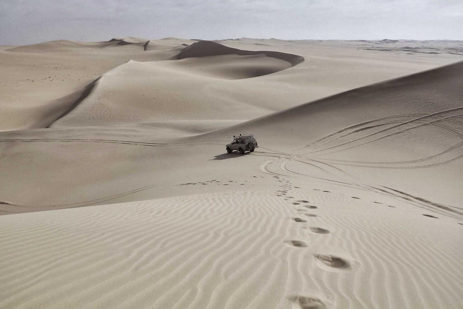Lone vehicle crossing vast rippled desert dunes