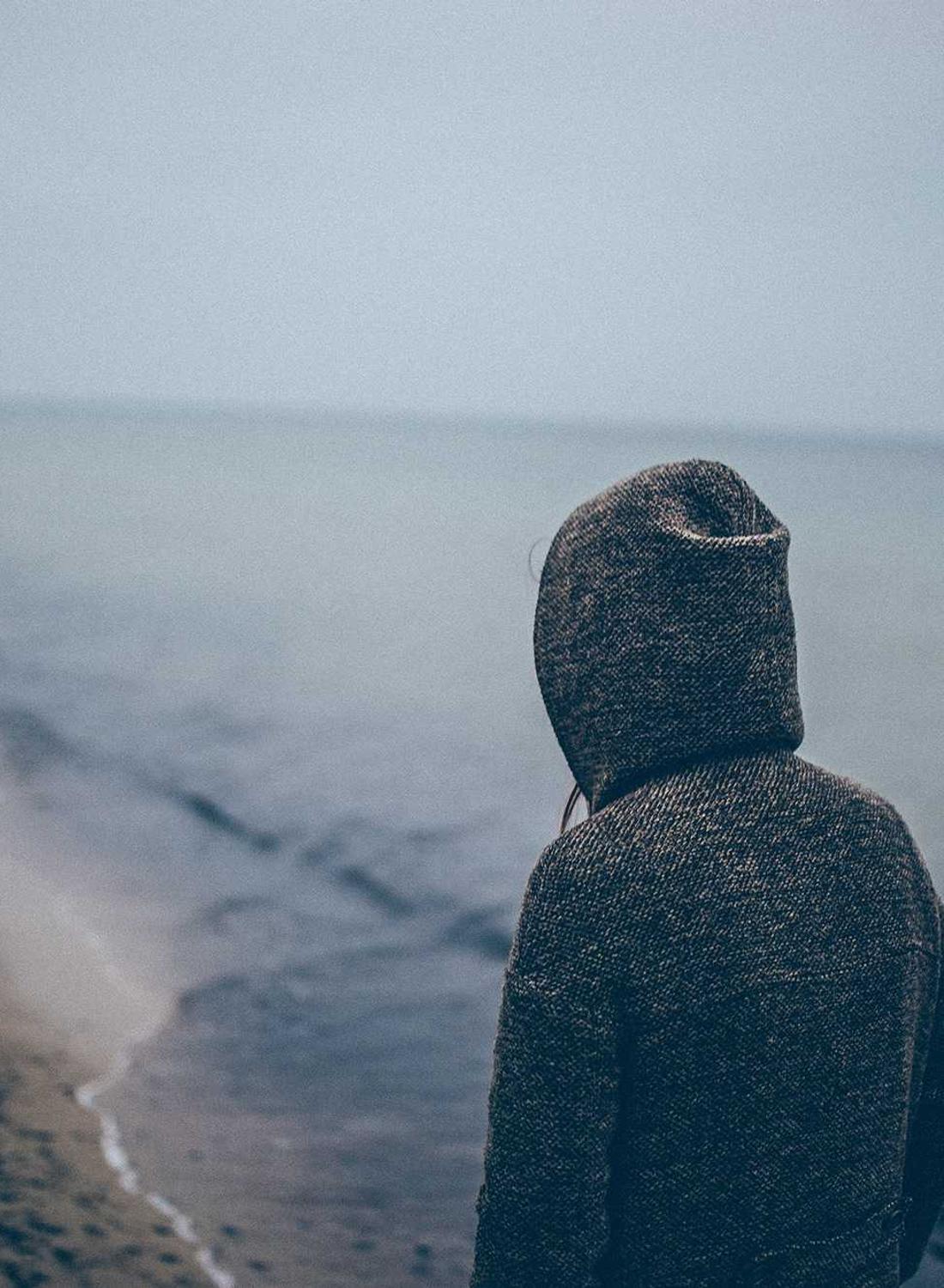 Solitary hooded figure facing a calm sea